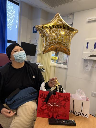 Kirah holds a golden star shaped ballooon with Congratulations message. She is surrounded by gift bags and though she is wearing a face mask you can tell she is smiling.