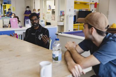 Comedian Romesh Ranganathan is sat at a table speaking to a young person