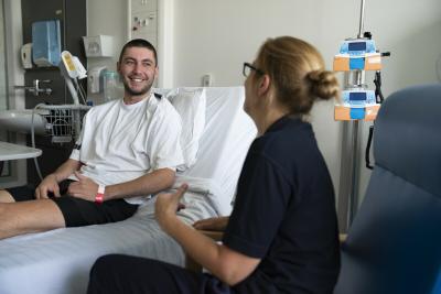 Young person on hospital bed talking with Teenage Cancer Trust nurse